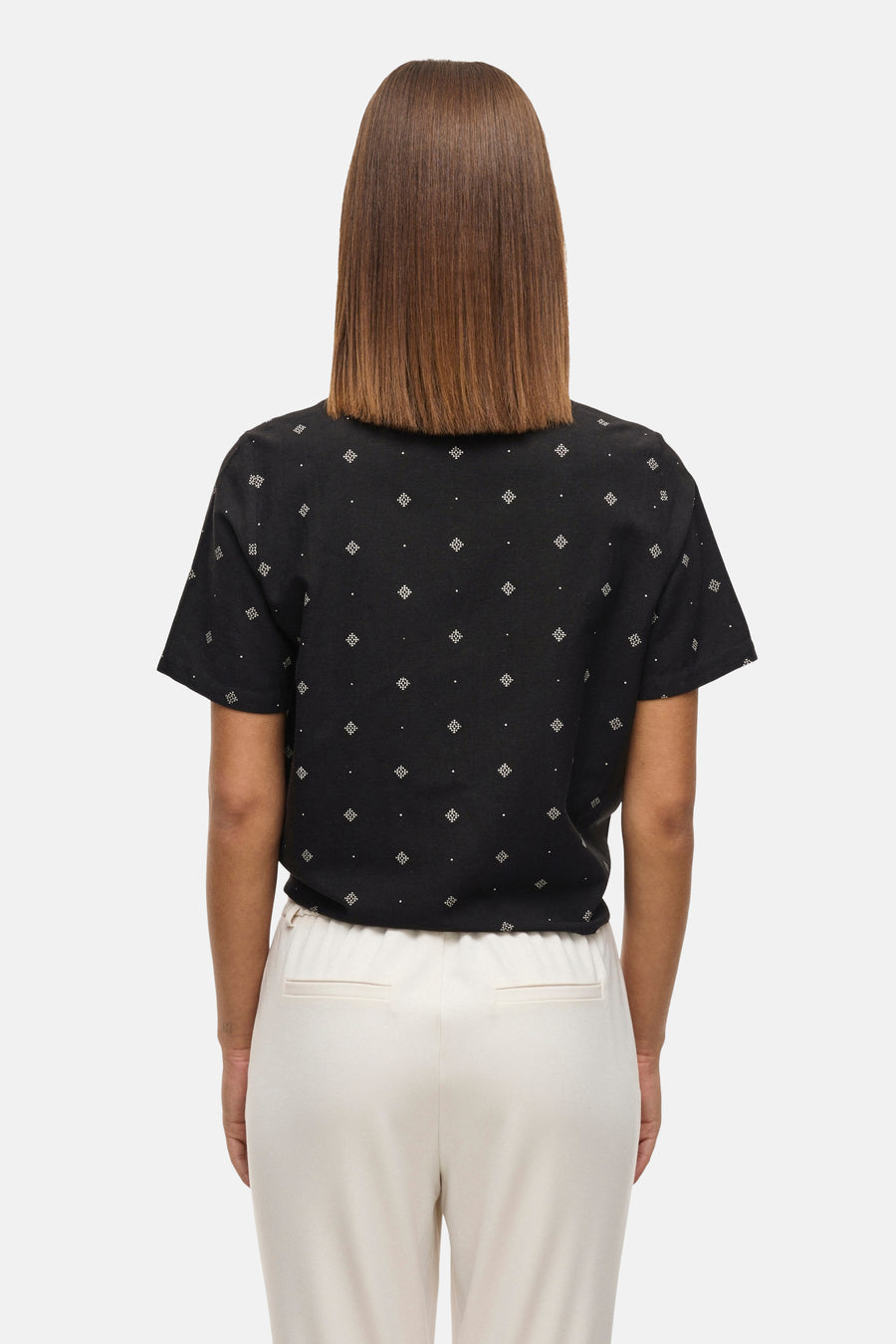 Zwarte blouse met korte mouwen van VILA®, met wit geometrisch patroon en witte broek.