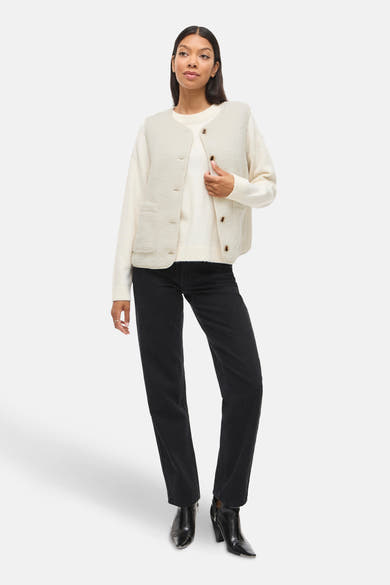 Gilet écru de VILA®, porté sur un pull blanc avec un jean noir et des bottines vernies.
