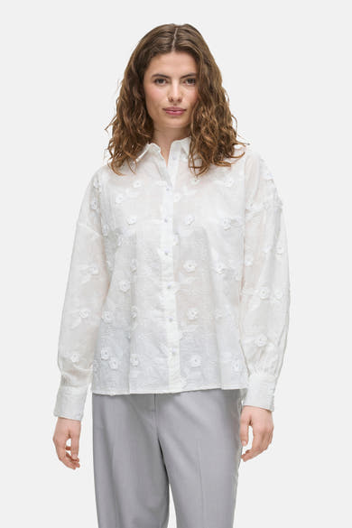 Wit overhemd met lange mouwen van VILA, met delicate bloemenborduursels, gedragen met een grijze broek.