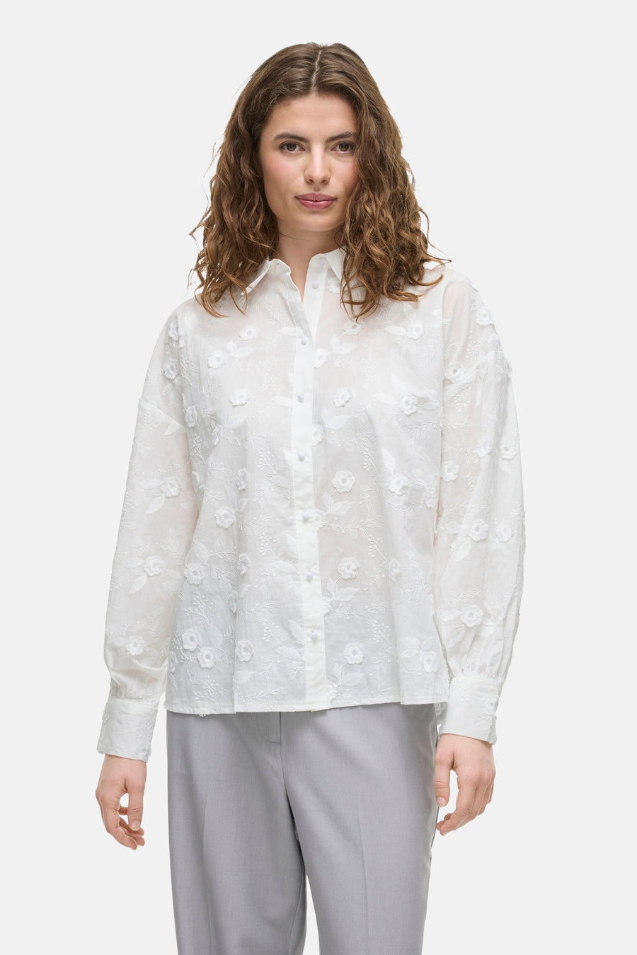 Wit overhemd met lange mouwen van VILA, met delicate bloemenborduursels, gedragen met een grijze broek.