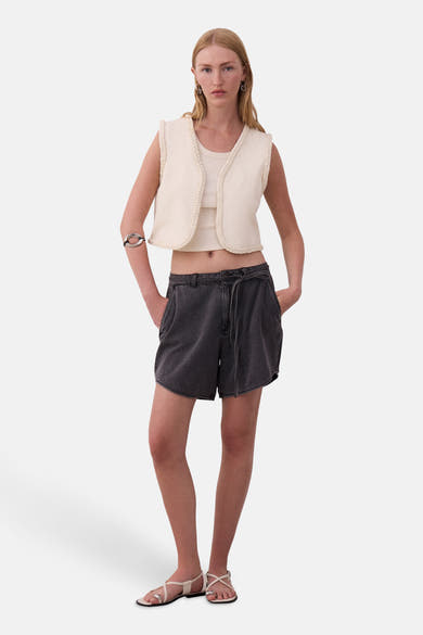 Korte grijze rok van VILA®, gedragen met een gebroken witte top en vest, en witte sandalen.