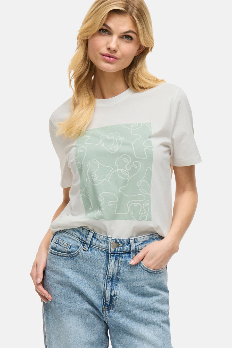 T-shirt à manches courtes blanc de VILA, avec un motif de visages abstraits et porté avec un jean.
