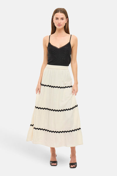 Jupe longue beige de VILA, à volants avec ourlets décoratifs noirs, portée avec un débardeur noir et des mules noires.