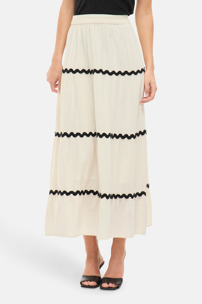 Jupe longue beige par VILA®, à volants avec motif ondulé noir, portée avec des chaussures noires à talons.