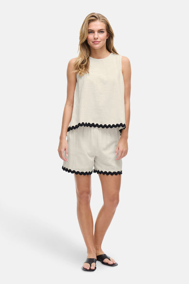 Ecru mouwloos hemd van VILA® met zwarte festonrand, gedragen met een bijpassende short en sandalen.
