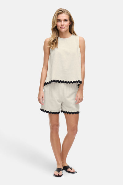 Ecru mouwloos hemd van VILA® met zwarte festonrand, gedragen met een bijpassende short en sandalen.
