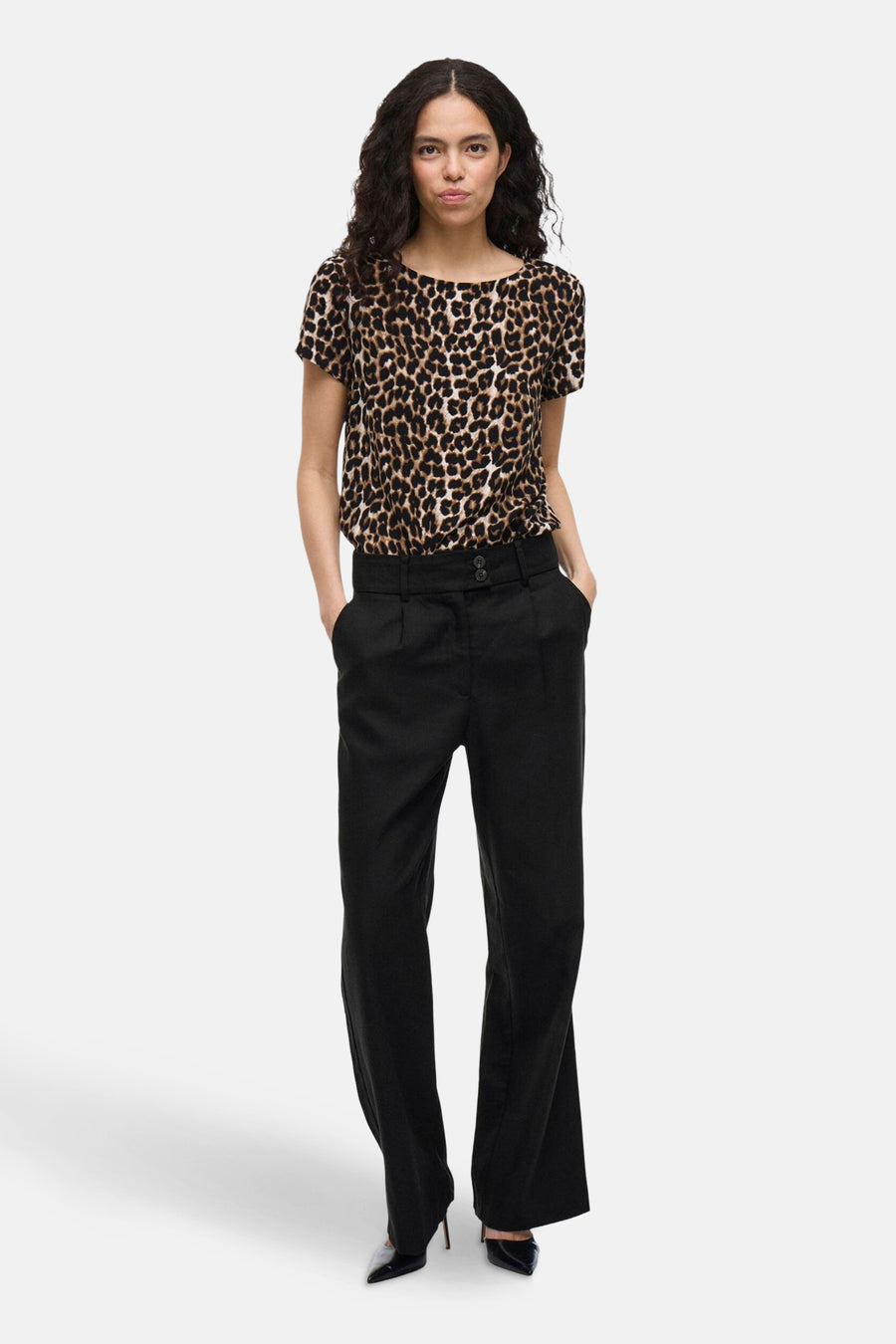 Pantalon de costume noir de VILA®, porté avec un chemisier imprimé léopard et des escarpins noirs vernis.
