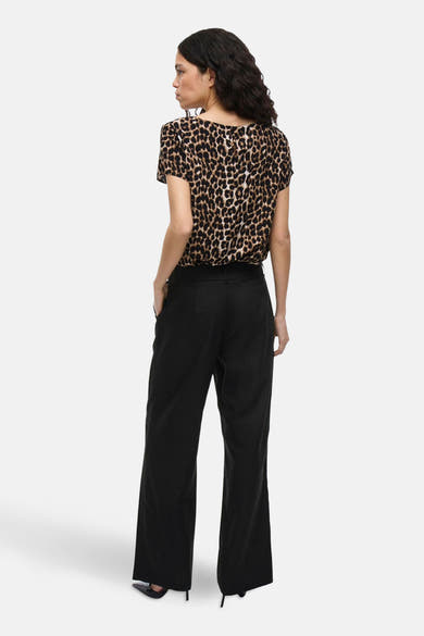 Pantalon de costume noir de VILA, ample, porté avec un chemisier à motif léopard et des escarpins noirs.
