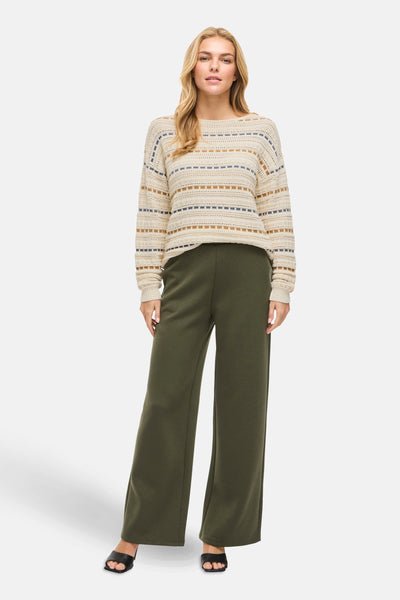 Pull à col rond beige de VILA®, à rayures bleues et marron, porté avec un pantalon vert olive et des sandales noires.
