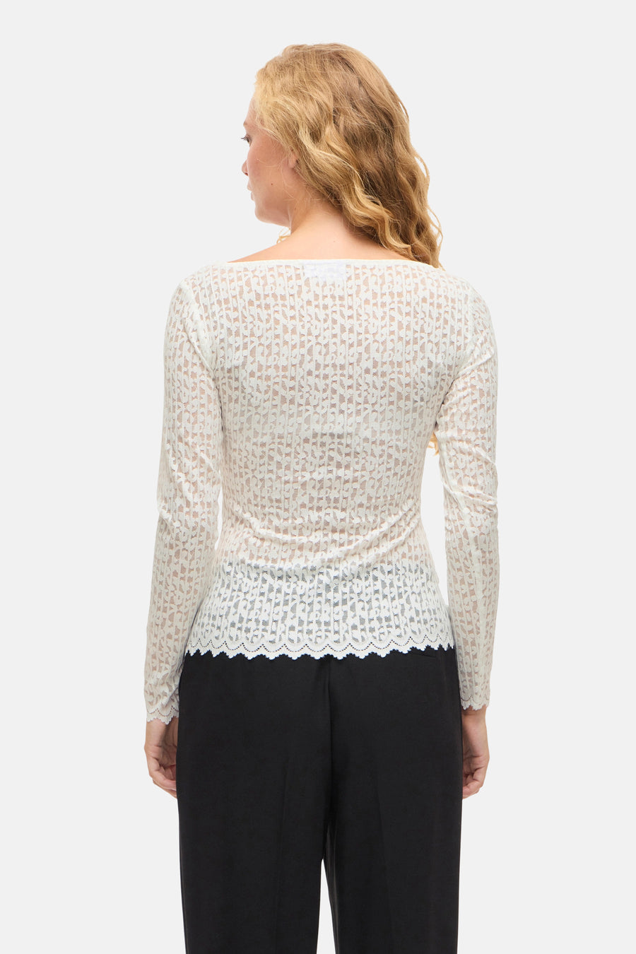 Witte T-shirt met lange mouwen van VILA, van doorschijnend bloemenkant, gedragen met een effen zwarte broek.
