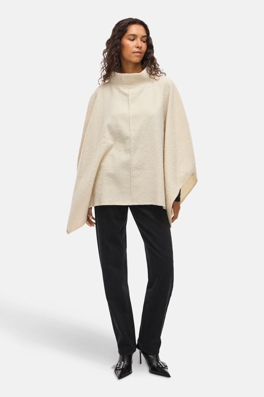 Beige poncho van VILA, gedragen met een zwarte broek en enkellaarsjes met gesp.