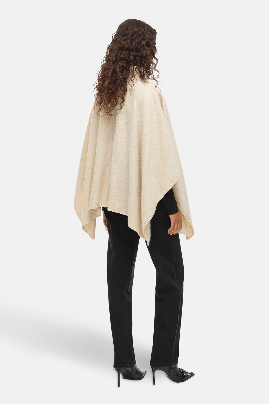 Beige poncho van VILA, gedragen met een zwarte trui en een zwarte flared jeans met puntige pumps.