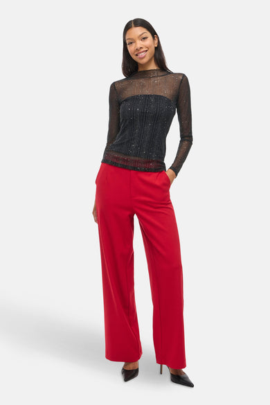 T-shirt à manches longues noir par VILA, avec paillettes argentées, porté avec un pantalon rouge et des talons aiguilles.