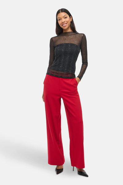 T-shirt à manches longues noir par VILA, avec paillettes argentées, porté avec un pantalon rouge et des talons aiguilles.