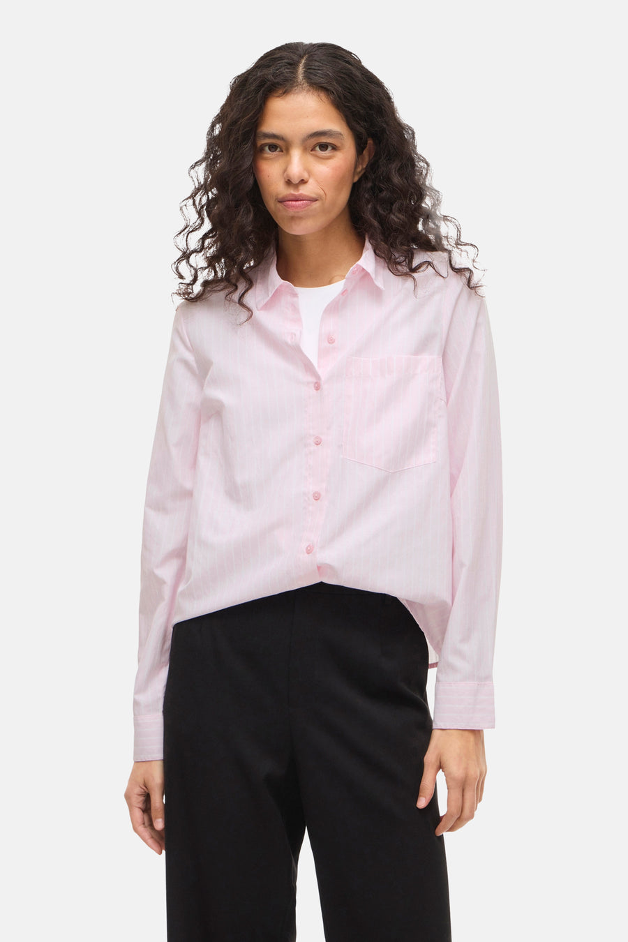 Chemise rose à rayures verticales de VILA, portée ouverte sur un t-shirt blanc et un pantalon noir.