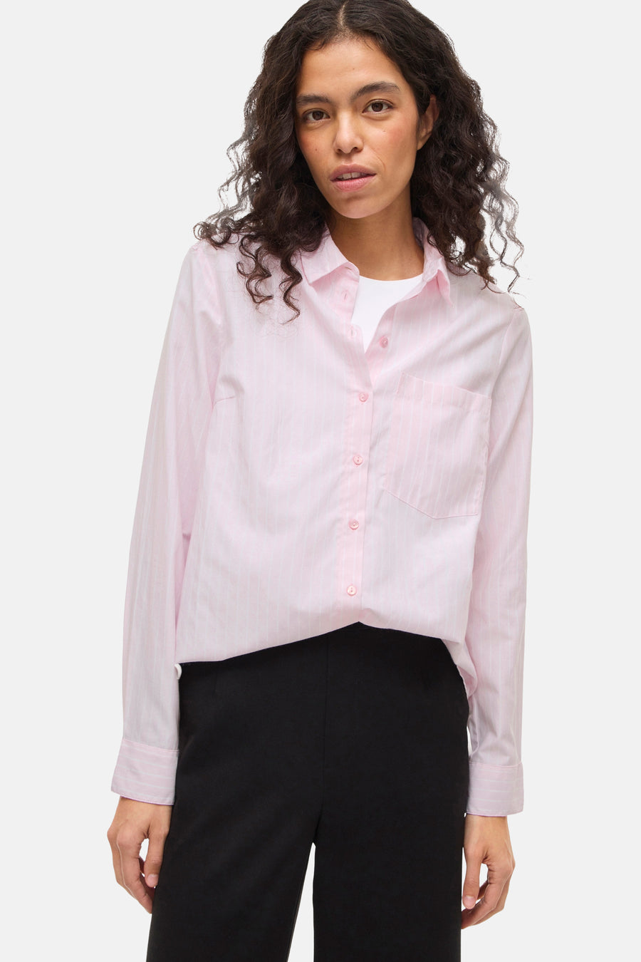 Chemise à manches longues rose rayée de VILA, portée sur un t-shirt blanc et un pantalon noir taille haute.