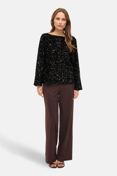 Blouse noire à manches longues de VILA®, ornée de paillettes brillantes, portée avec un pantalon marron et des sandales.