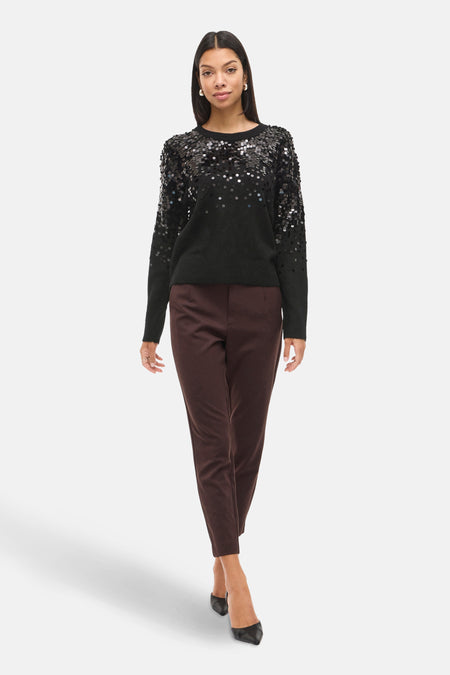 Pull col rond noir par VILA orné de paillettes argentées sur le haut, porté avec un pantalon marron et des escarpins noirs.