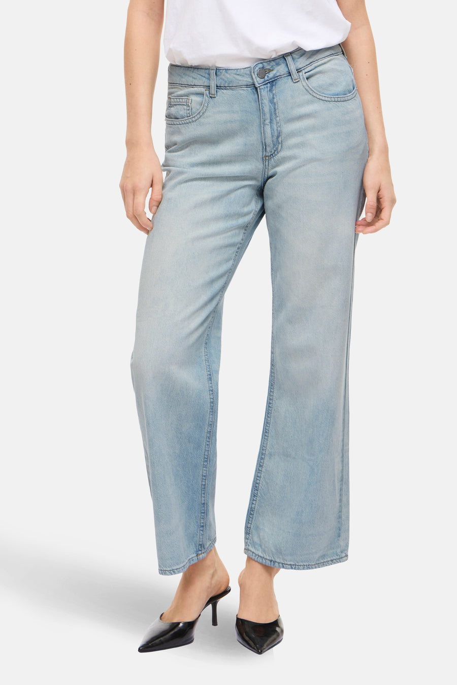 Wijde spijkerbroek in lichtblauw denim van VILA, gedragen met een wit T-shirt en zwarte puntige pumps.