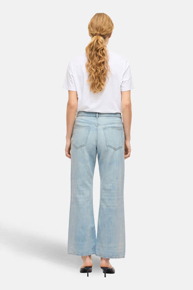 Lichtblauwe wijde jeans van VILA, gedragen met een wit T-shirt en zwarte hakken, van achteren gezien.