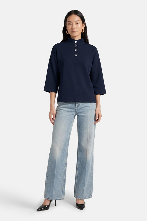 Sweat bleu par VILA, avec col montant à boutons et manches trois quarts, porté avec un jean ample et des escarpins noirs.

