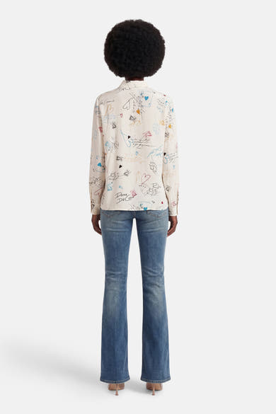 Chemise à manches longues multicolore de VILA®, avec des motifs de cartes à jouer et des écritures, portée avec un jean évasé.
