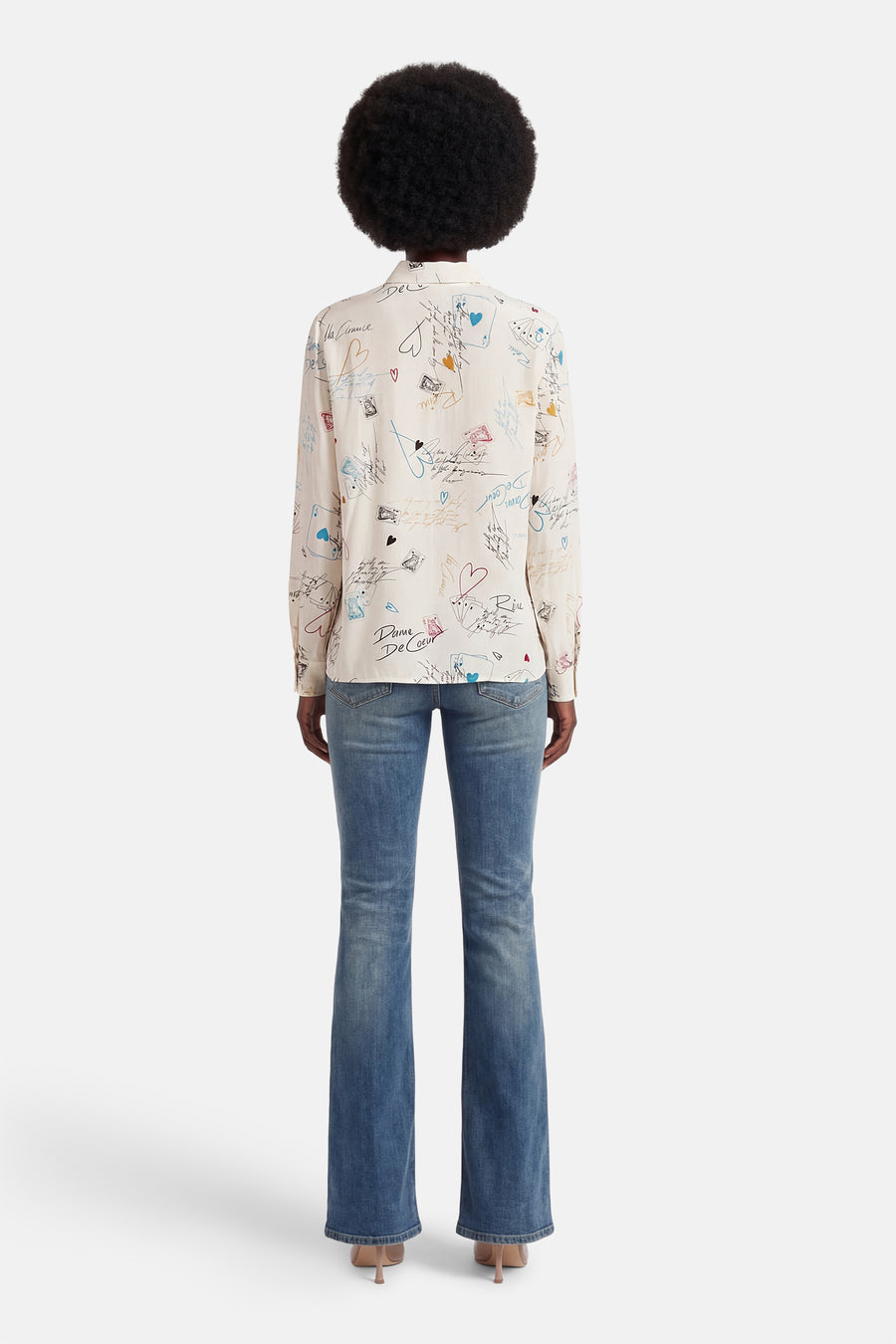 Chemise à manches longues multicolore de VILA®, avec des motifs de cartes à jouer et des écritures, portée avec un jean évasé.

