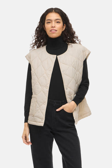 Beige mouwloos vest van VILA® met doorgestikt patroon en opgestikte zakken, gedragen met een zwarte trui en een spijkerbroek.