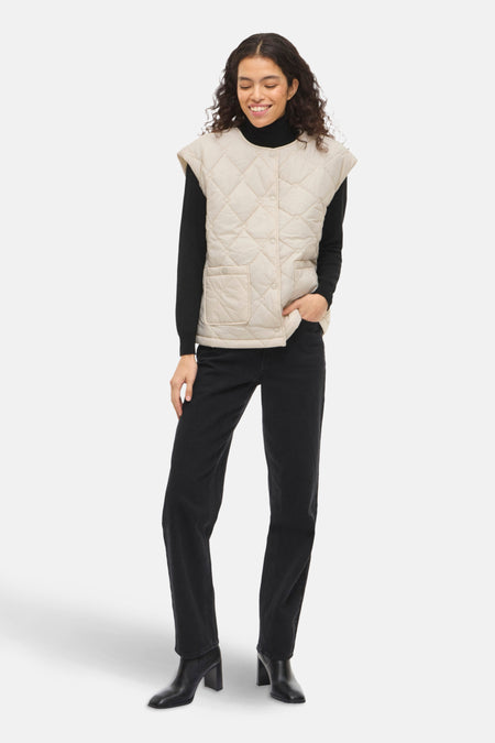 Veste sans manches beige de VILA®, matelassée à motif losanges, portée sur un pull noir avec un jean noir.