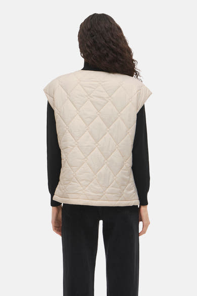 Beige mouwloos vest van VILA, met doorgestikt ruitpatroon, gedragen over een zwarte trui en een zwarte jeans, van achteren gezien.