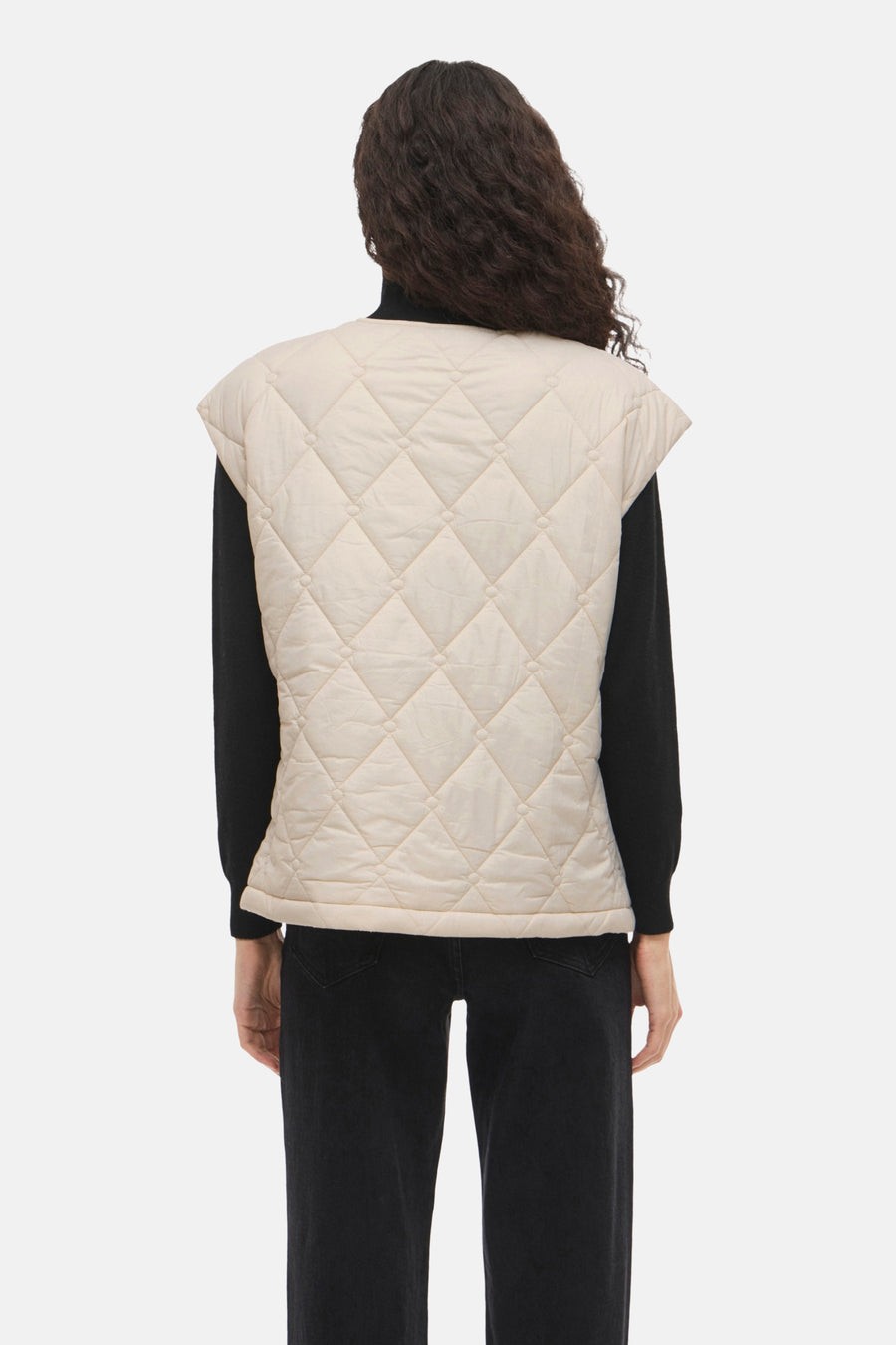 Beige mouwloos vest van VILA, met doorgestikt ruitpatroon, gedragen over een zwarte trui en een zwarte jeans, van achteren gezien.