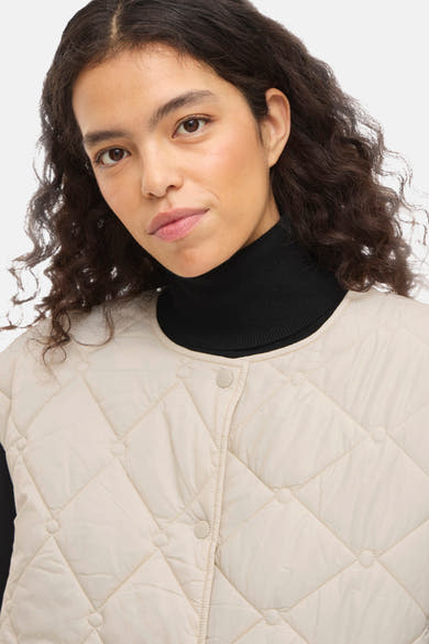 Beige mouwloos gewatteerd vest met ruitpatroon van VILA, gedragen over een zwarte coltrui.