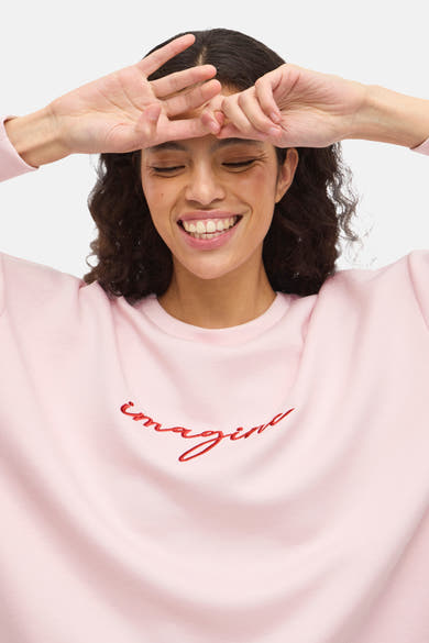 Zweetshirt van VILA® met de tekst 'imagine' in rood geborduurd op de voorkant, gedragen door een lachende mannequin.