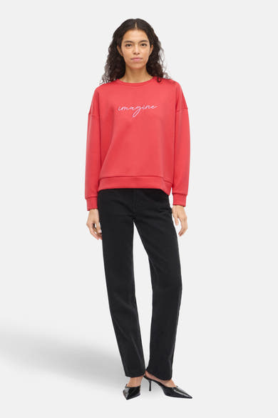 Sweat orange VILA® avec motif « Imagine » brodé, porté avec un jean noir et des escarpins noirs à talons aiguilles.