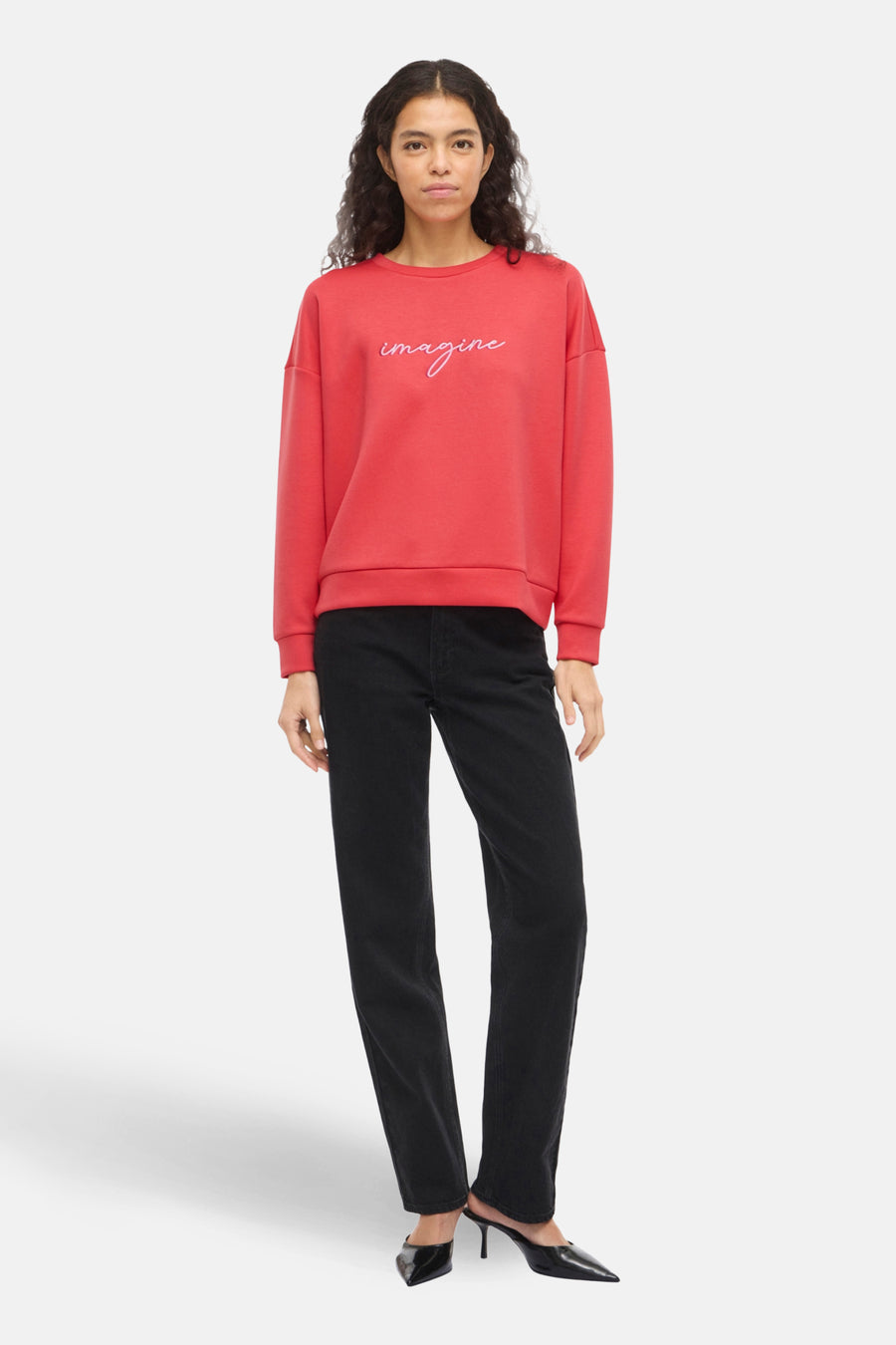 Sweat orange VILA® avec motif « Imagine » brodé, porté avec un jean noir et des escarpins noirs à talons aiguilles.