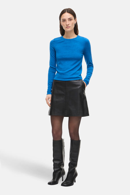 T-shirt à manches longues bleu de ROUGE EDIT, porté avec une jupe noire et des bottes en cuir.
