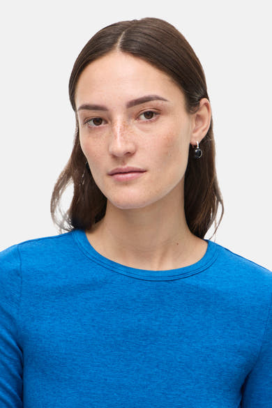 T-shirt à manches longues bleu de ROUGE EDIT, porté par une femme aux cheveux bruns, avec des boucles d'oreilles.