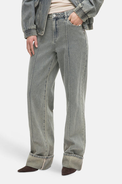 Jean large bleu clair de ROUGE EDIT, avec coutures verticales apparentes et revers aux chevilles, porté avec des chaussures marron.
