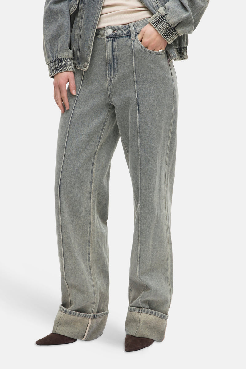 Jean large bleu clair de ROUGE EDIT, avec coutures verticales apparentes et revers aux chevilles, porté avec des chaussures marron.
