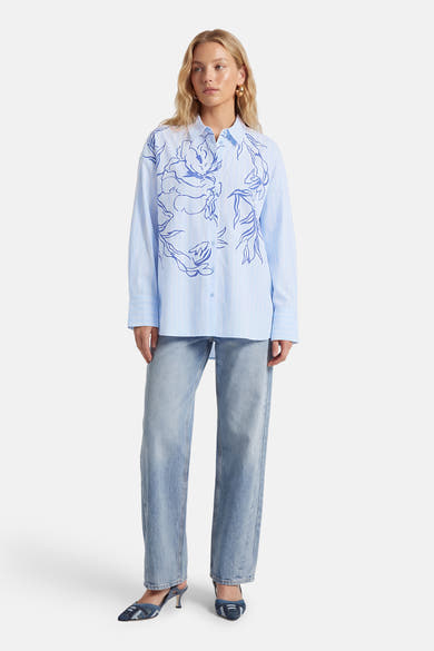 Chemise à manches longues bleue rayée de VILA®, ornée de motifs floraux bleus, portée avec un jean et des escarpins.
