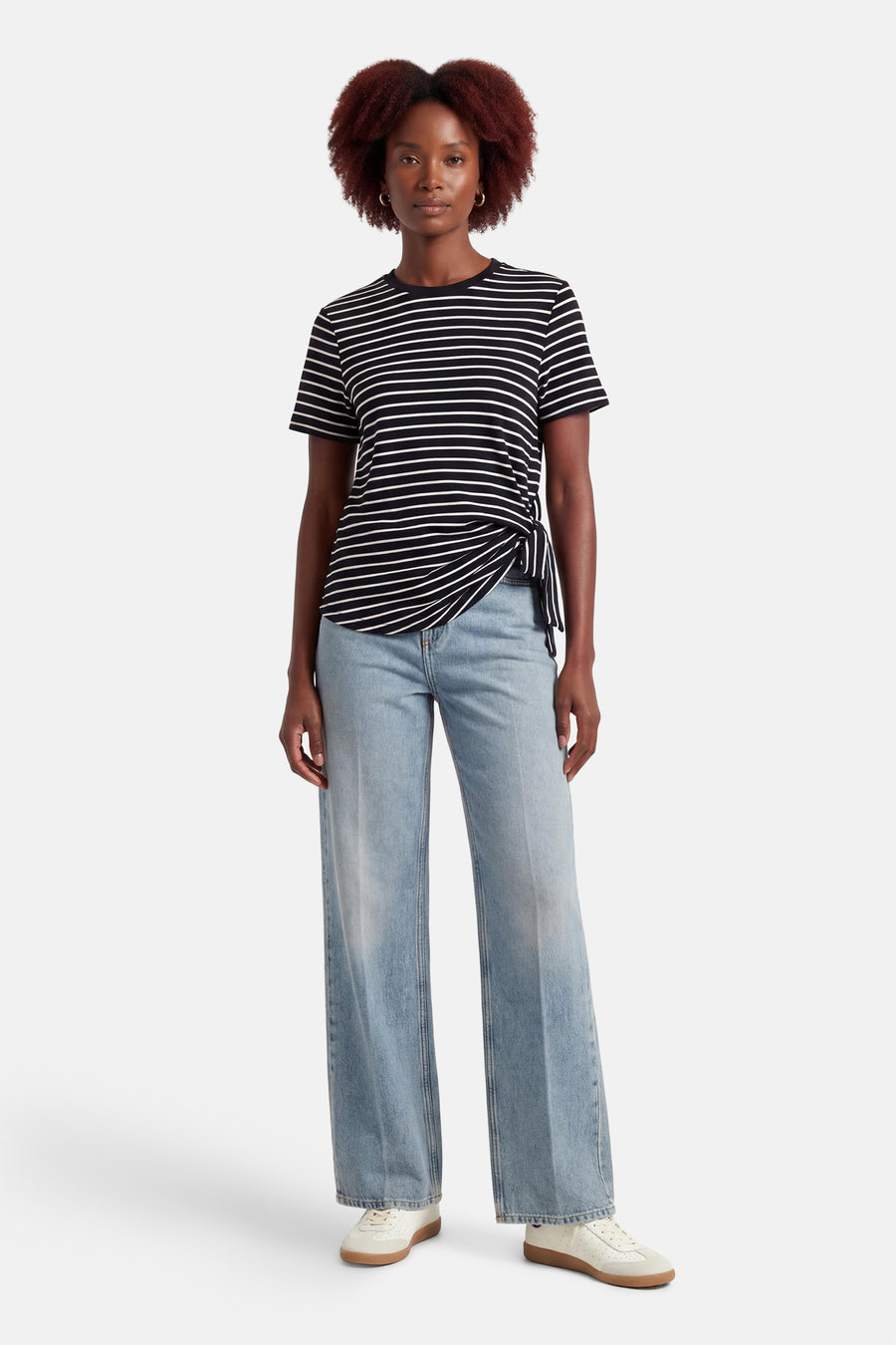 T-shirt à manches courtes noir rayé by VILA®, avec un nœud décoratif sur le côté, porté avec un jean décontracté.
