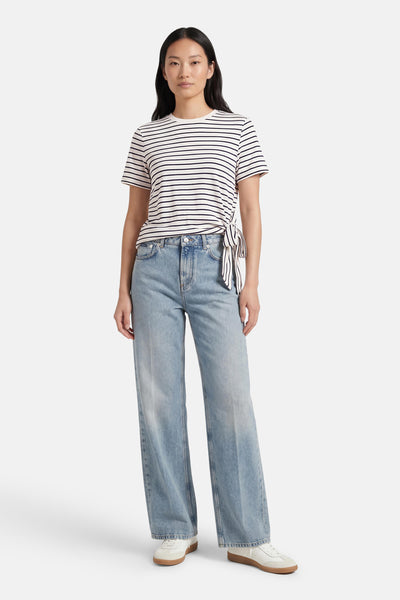 T-shirt à manches courtes blanc à rayures noires de VILA®, noué sur le côté et porté avec un jean ample bleu.