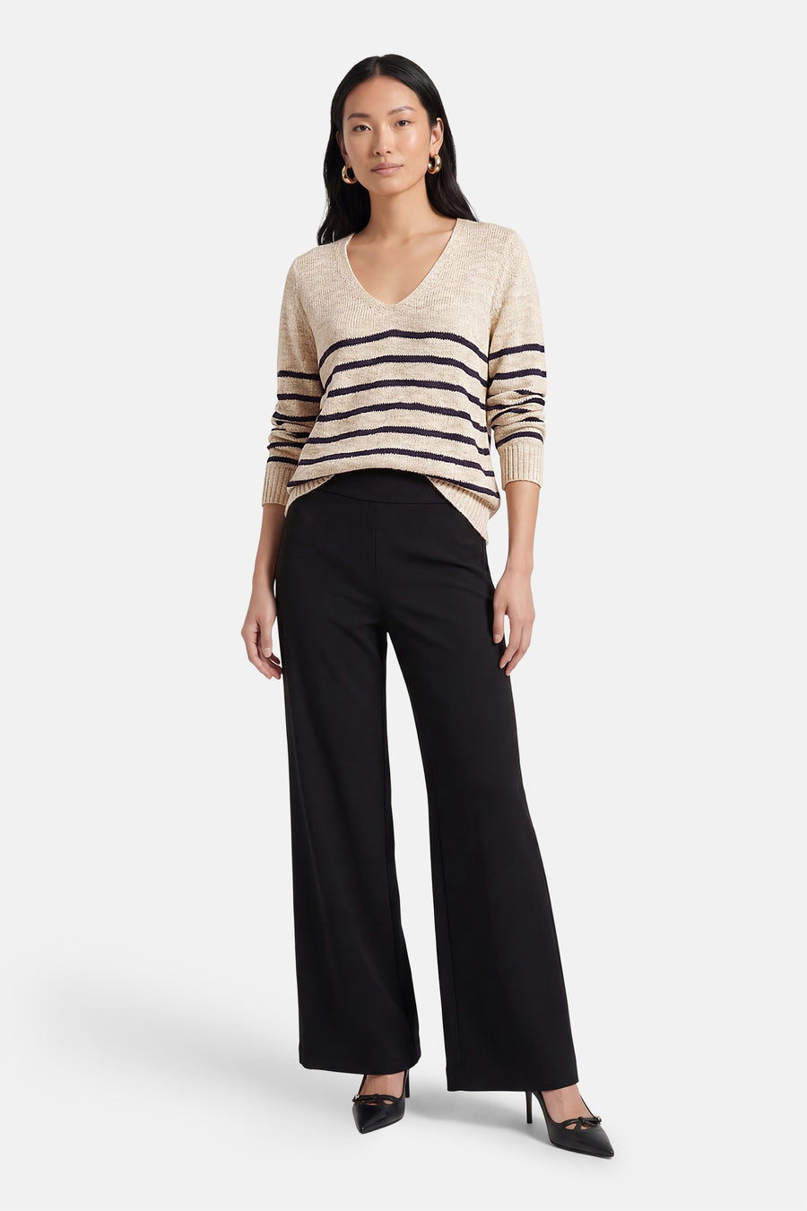 Pull à col en V multicolore de VILA®, avec des rayures horizontales, porté avec un pantalon noir évasé et des escarpins noirs.
