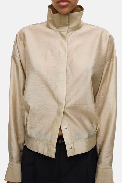 Chemise à manches longues beige de ROUGE EDIT, à col montant et détails boutonnés, portée avec un pantalon noir.
