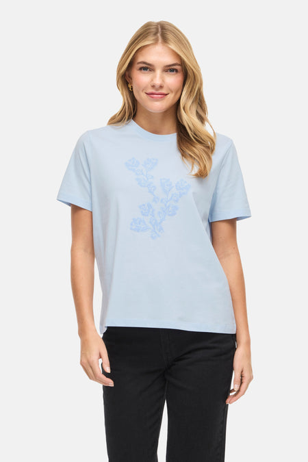 Blauw T-shirt met korte mouwen van VILA, met een bloemenprint, gedragen met een zwarte jeans en pumps.