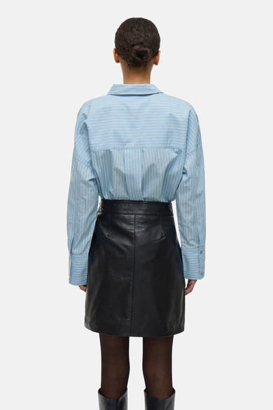 Chemise à manches longues bleue rayée de ROUGE EDIT, portée avec une jupe noire en cuir, vue de dos.
