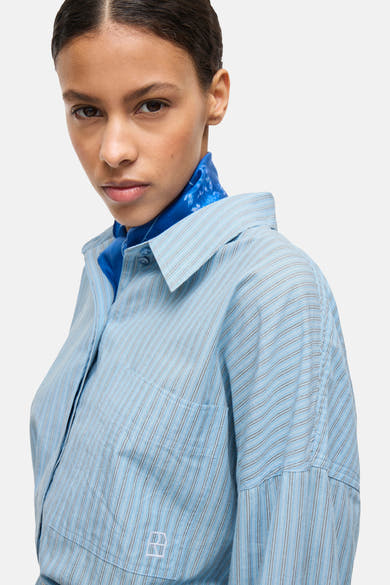 Chemise à manches longues bleue à rayures, de ROUGE EDIT, avec un foulard bleu autour du cou.