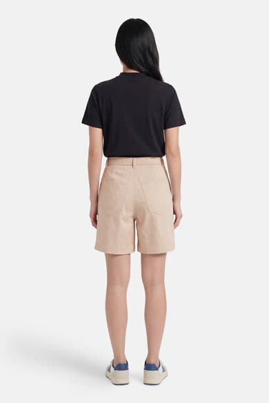 Short beige de VILA®, vue de dos, avec taille haute et poches, porté avec un t-shirt noir et des baskets.