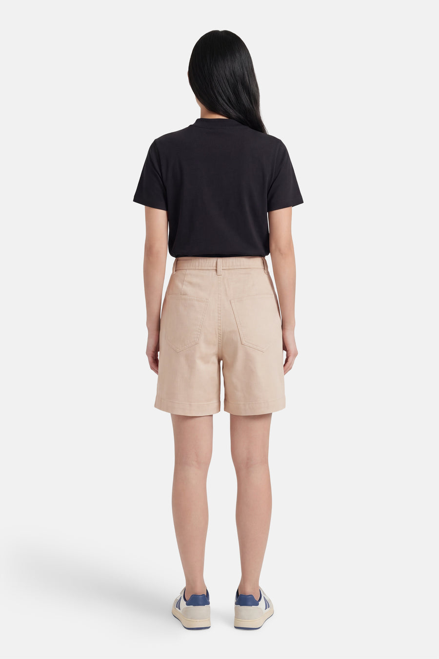 Short beige de VILA®, vue de dos, avec taille haute et poches, porté avec un t-shirt noir et des baskets.
