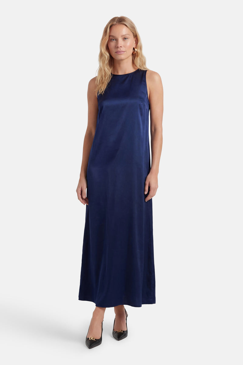 Robe longue bleue soyeuse de VILA® sans manches, encolure ronde, portée avec des talons noirs à boucle dorée.